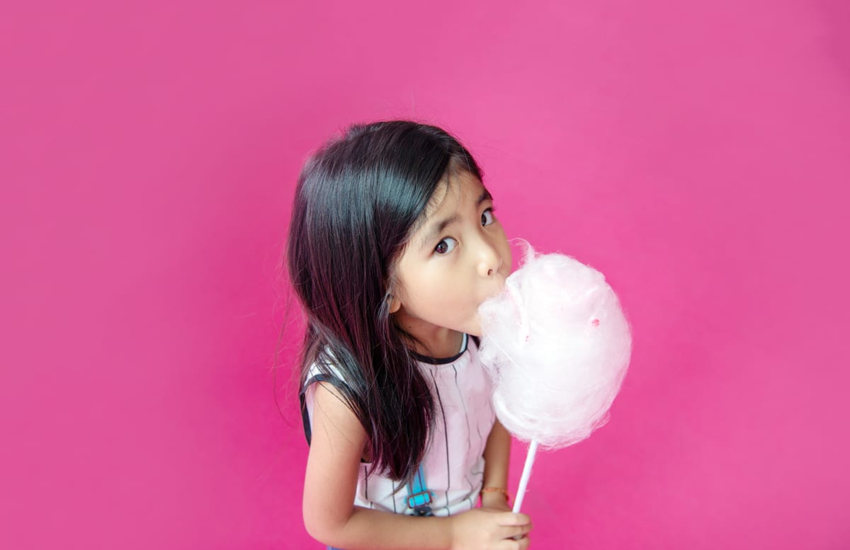 Candy Floss Machine hire — little girl enjoys cotton candy on pink background | Panda Party Hire Hire candy floss machine — little girl enjoys cotton candy on pink background for parties and events in Johannesburg, Sandton and Randburg