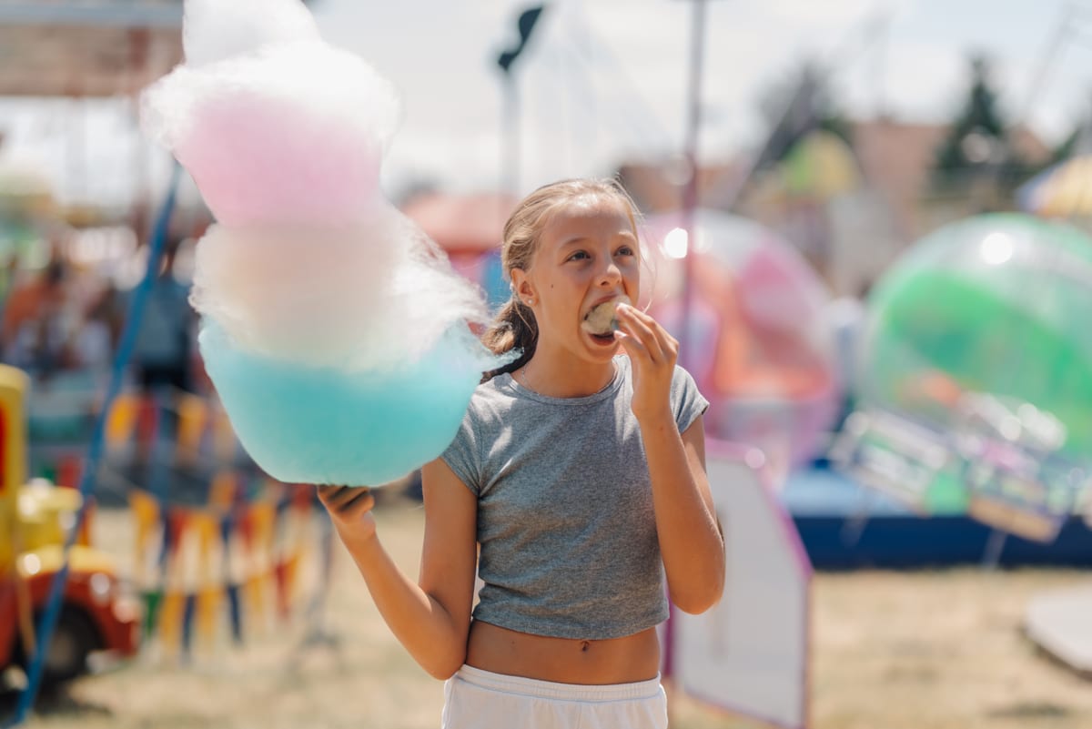 Candy Floss Machine hire — girl eating cotton candy and pastry at amusement p | Panda Party Hire Hire candy floss machine — girl eating cotton candy and pastry at amusement p for parties and events in Johannesburg, Sandton and Randburg