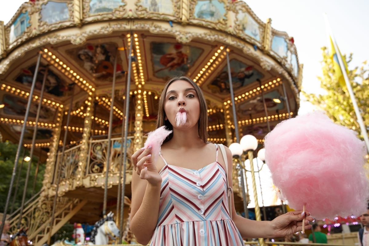Candy Floss Machine hire — woman enjoys pink cotton candy near carousel | Panda Party Hire Hire candy floss machine — woman enjoys pink cotton candy near carousel for parties and events in Johannesburg, Sandton and Randburg