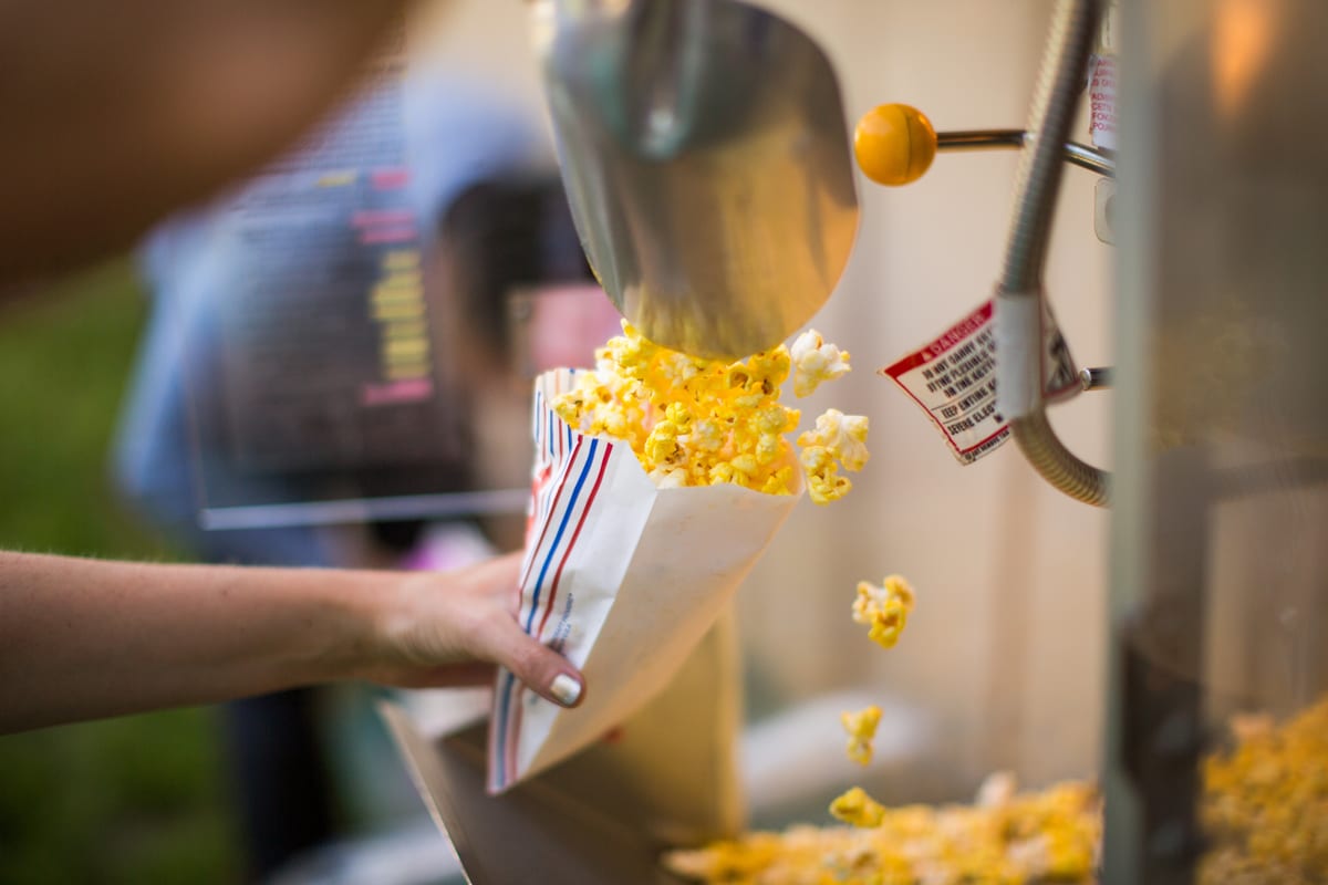 Popcorn machine hire — serving popcorn from hire machine | Panda Party Hire Hire popcorn machine — fresh popcorn scooped from a commercial hire machine into striped paper bags